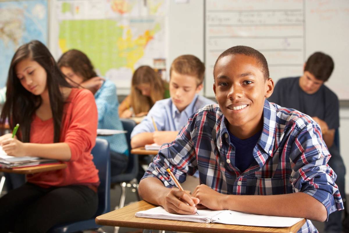 A boy is sitting at his desk in front of some other students.