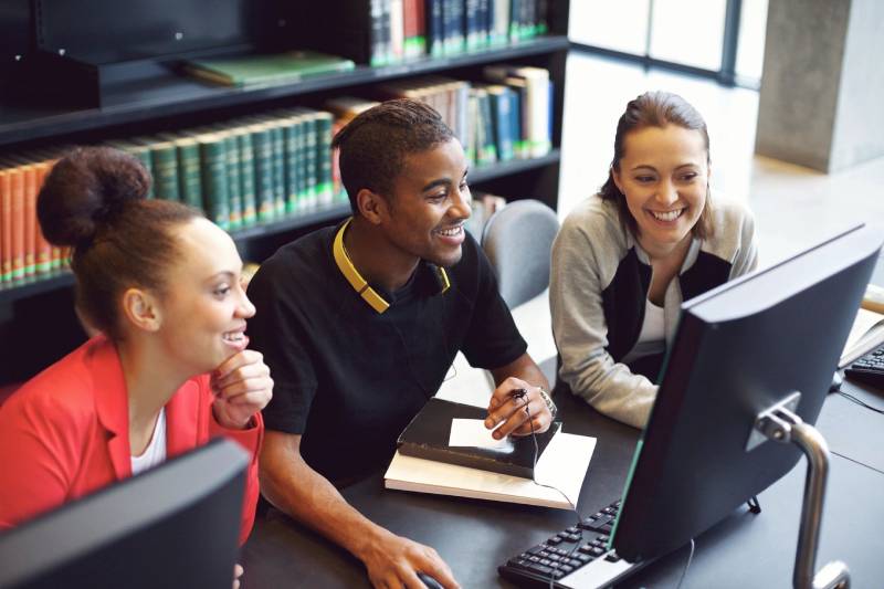 Three people sitting at a table with a computer.