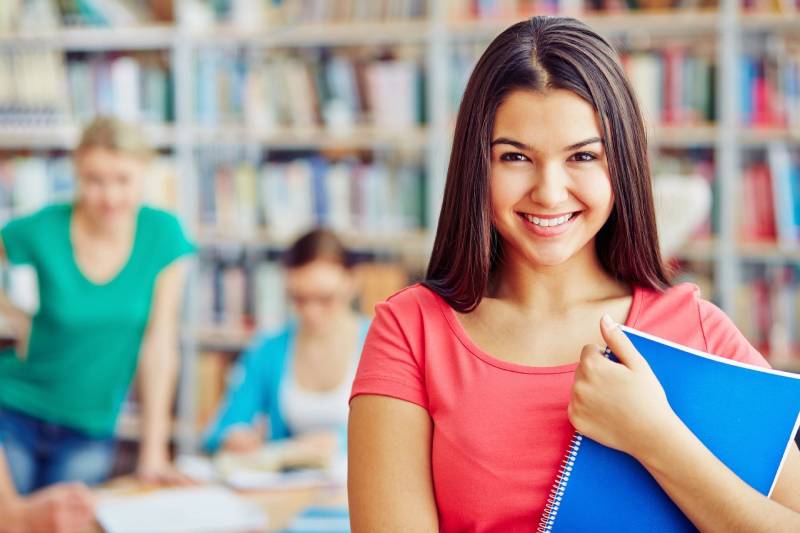 A girl is smiling while holding her book.