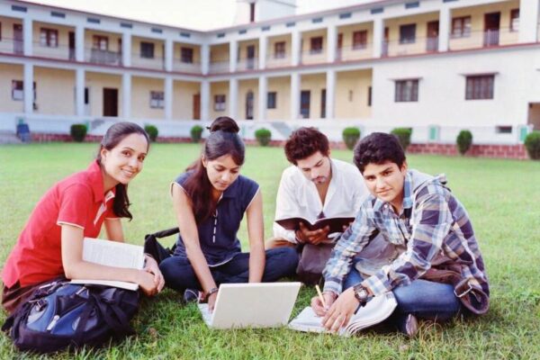 A group of people sitting on the grass with books and laptop