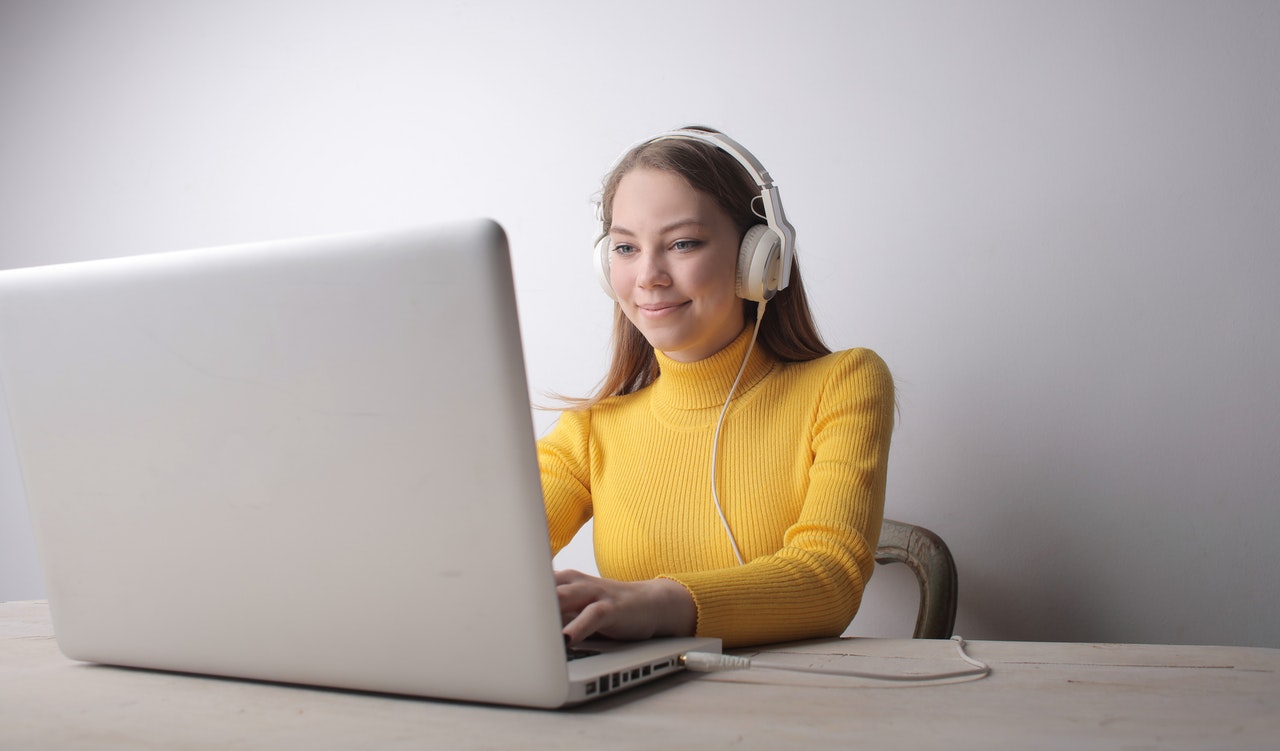 A woman wearing headphones sitting at a table with a laptop.